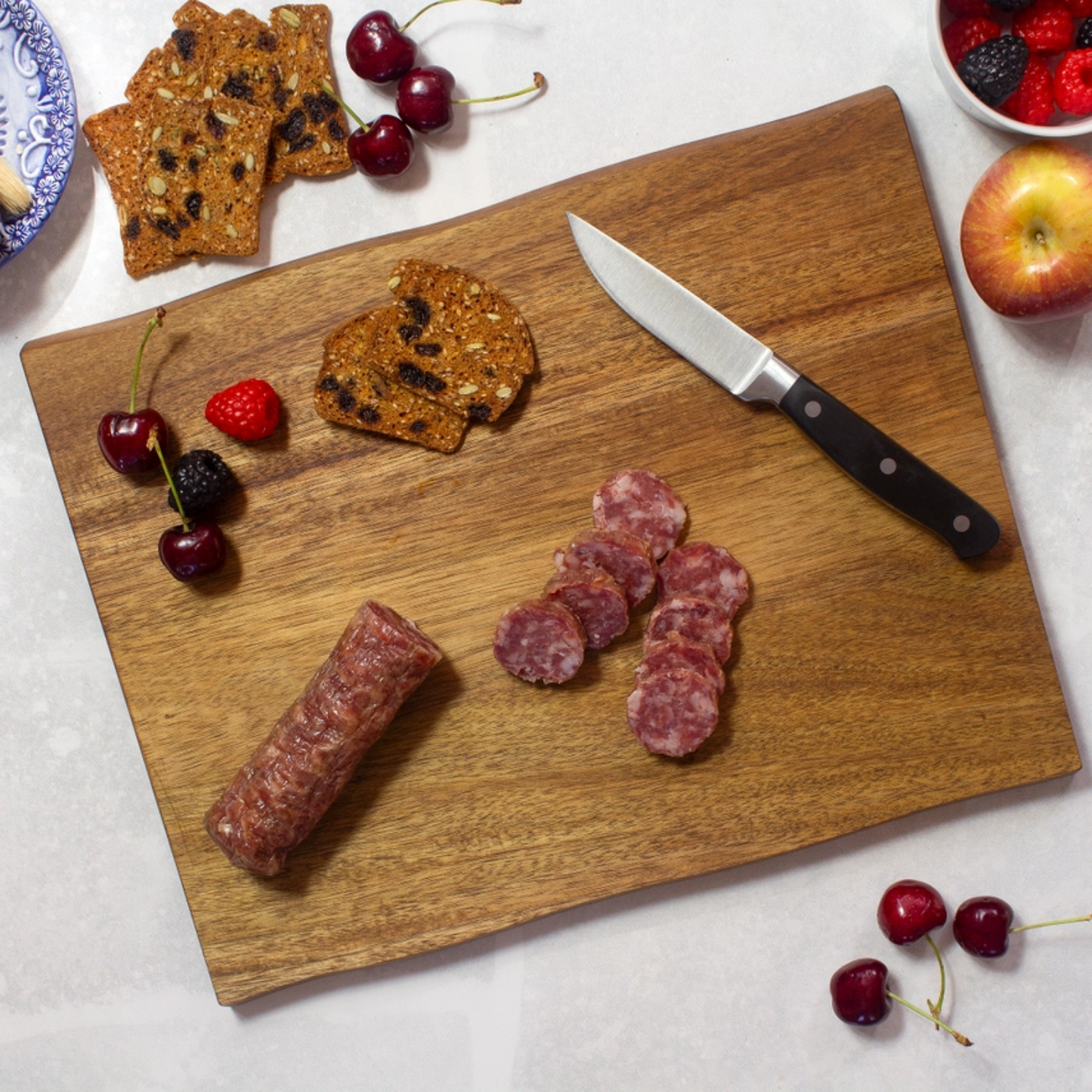 Acacia wood live edge serving board with cheese, salami, crackers, and fruit arranged for charcuterie display.