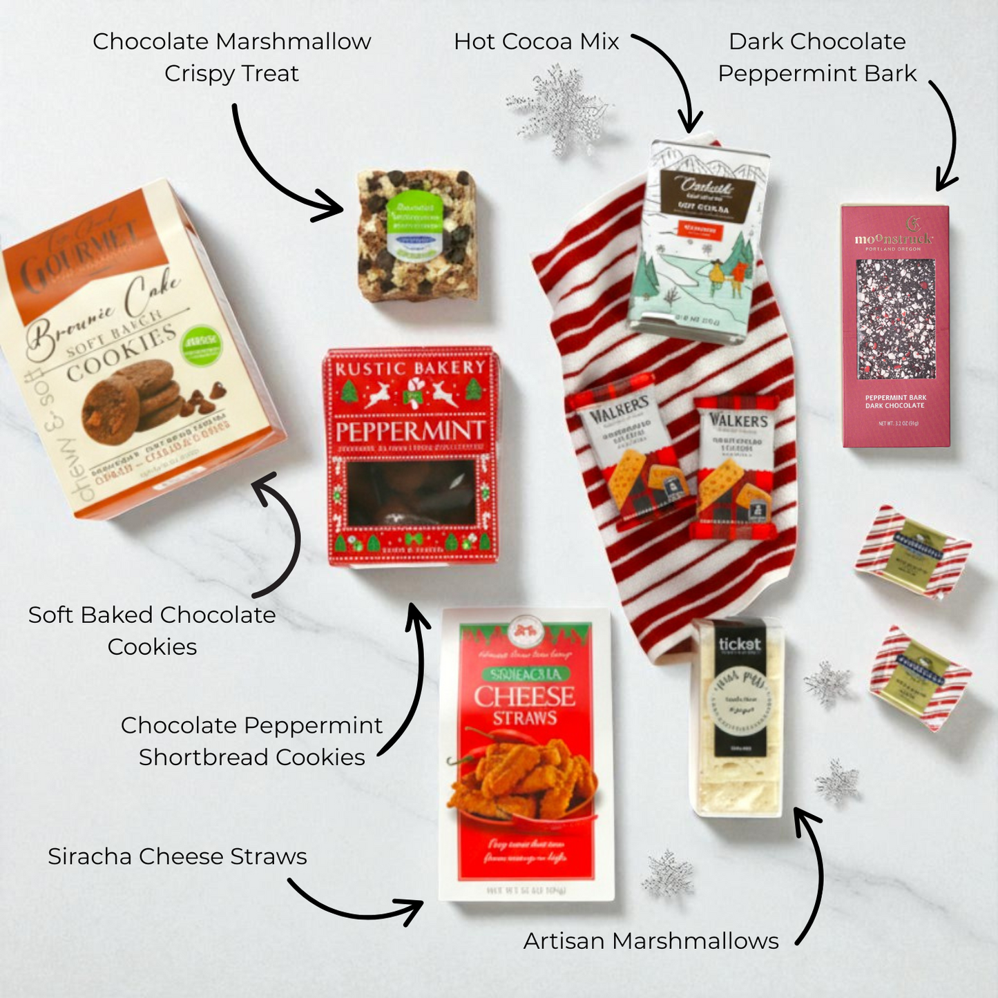 top down view of all of the snacks in the merry and bright gift basket including: cocoa mix, chocolate peppermint bark, chocolate shortbread cookies, siracha cheese straws and gourmet marshmallows