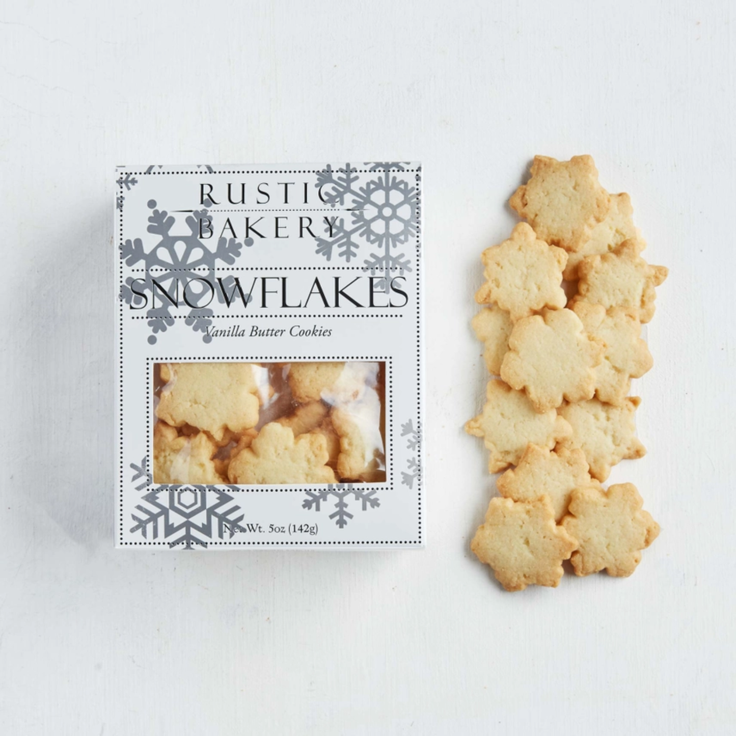 Snowflake-shaped cookies next to their packaging labeled 'Rustic Bakery Snowflakes' on a white background