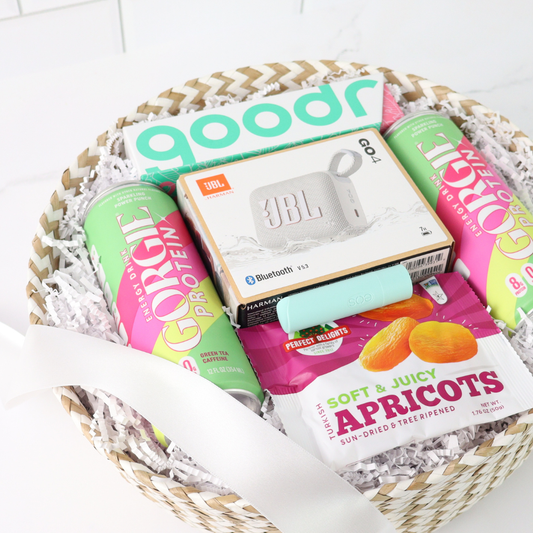 Close-up of a summer corporate team gift basket featuring gourmet snacks, sparkling protein drinks, a JBL speaker, white crinkle paper filler, and a branded appreciation card.