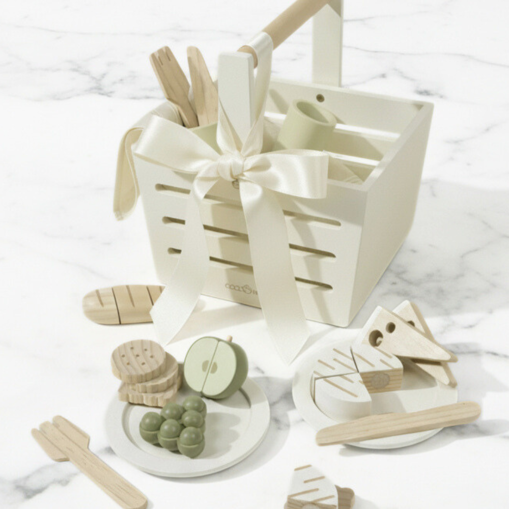 Wooden toys including a boat, fruits, and a basket with a bow on a white marble surface.