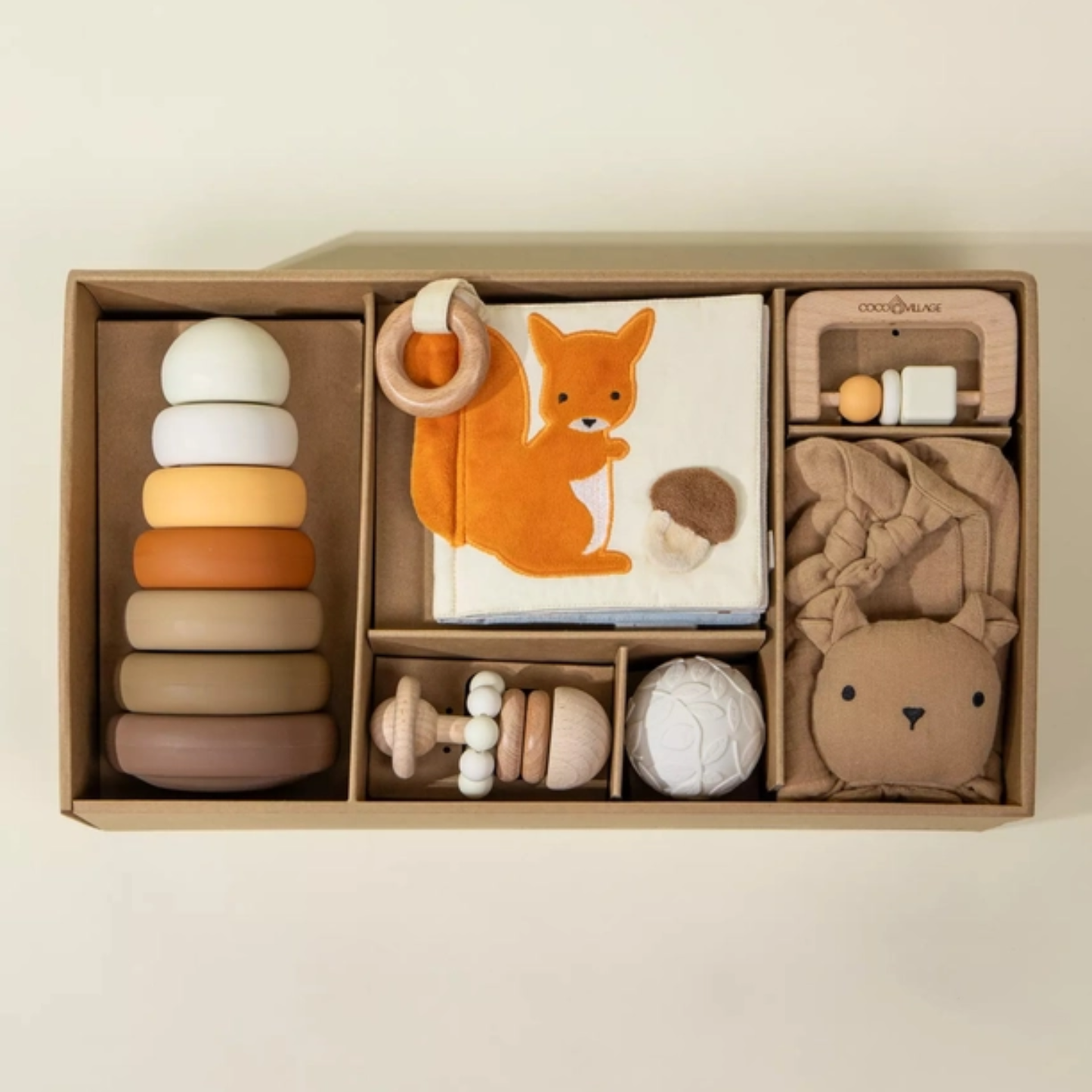 Neutral baby gift box with wooden rattle, silicone stacking tower, lovey, and woodland sensory book arranged in a kraft box.