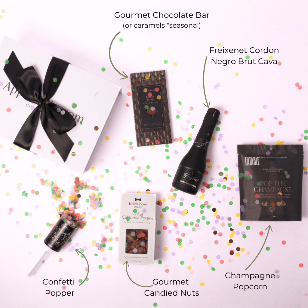 A top-down view of a celebration gift box with all items displayed: champagne popcorn, a Freixenet mini bottle, a gourmet chocolate bar, a festive confetti popper, and candied nuts.