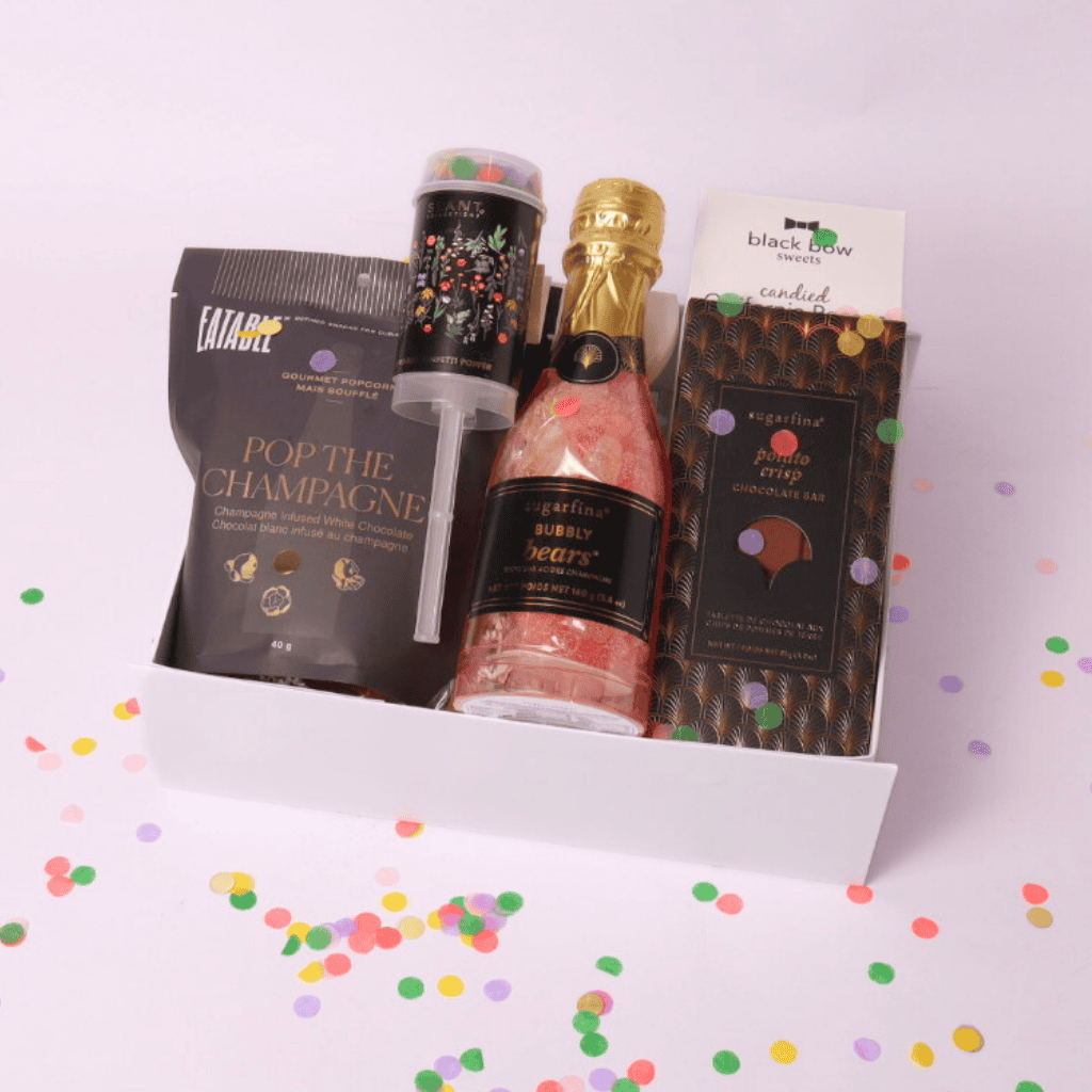 Luxury celebration gift box featuring champagne-infused popcorn, Sugarfina treats, a confetti popper, and a mini bottle of bubbly gummy bears.