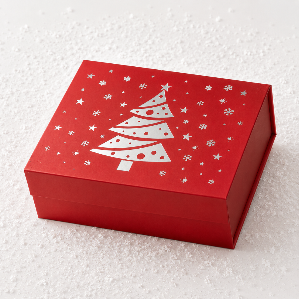 A red square gift box with a white Christmas tree and snowflake design on the lid, photographed on a white textured surface.