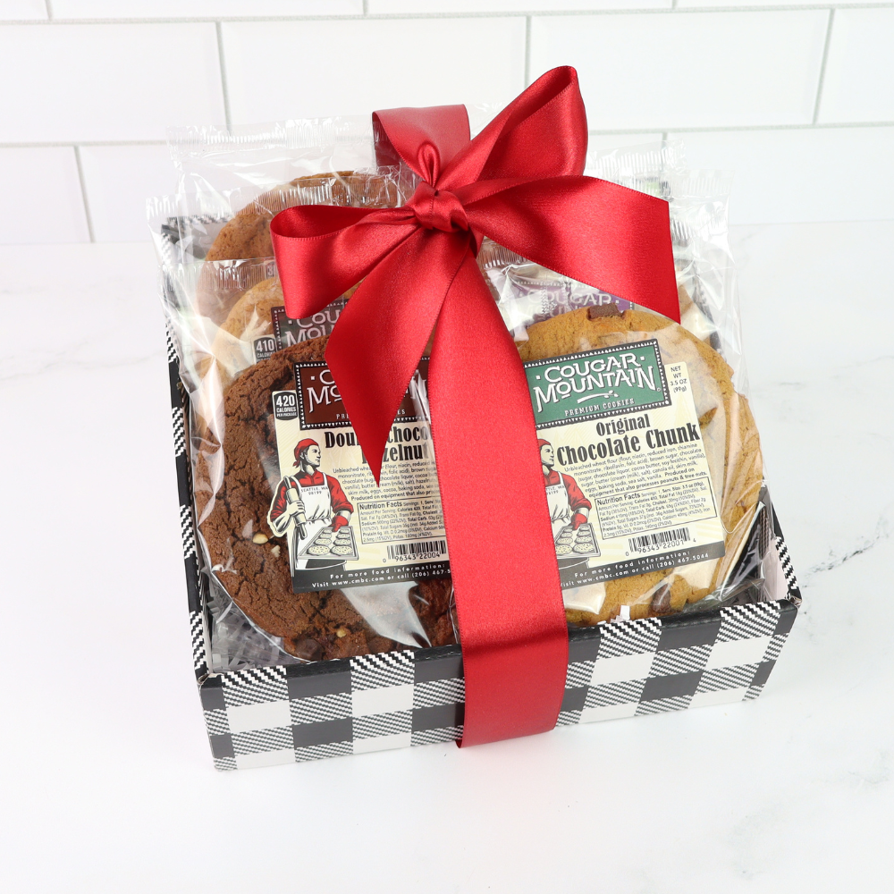 Packaged cookies with a red ribbon on a white tiled background.  Giant Cougar Mountain Cookies are 5 inches in diameter and are the size of your hand.  The weigh a whopping 3.5oz. equal to almost 4 regular cookies