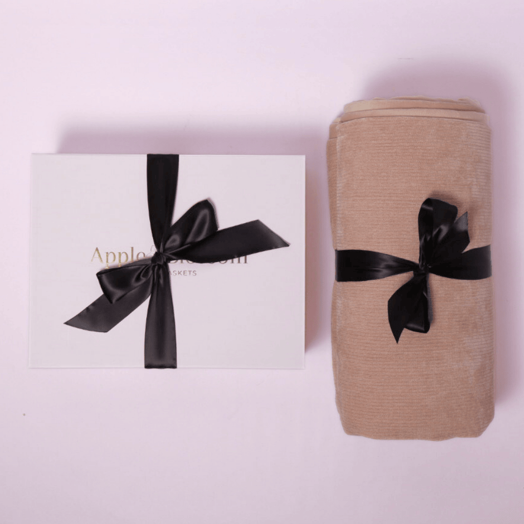 A luxury housewarming gift box featuring a plant-based cleaner, dish soap, candle, luxe throw, cookies, sponges, and a scrub brush, all elegantly presented in a signature white box.