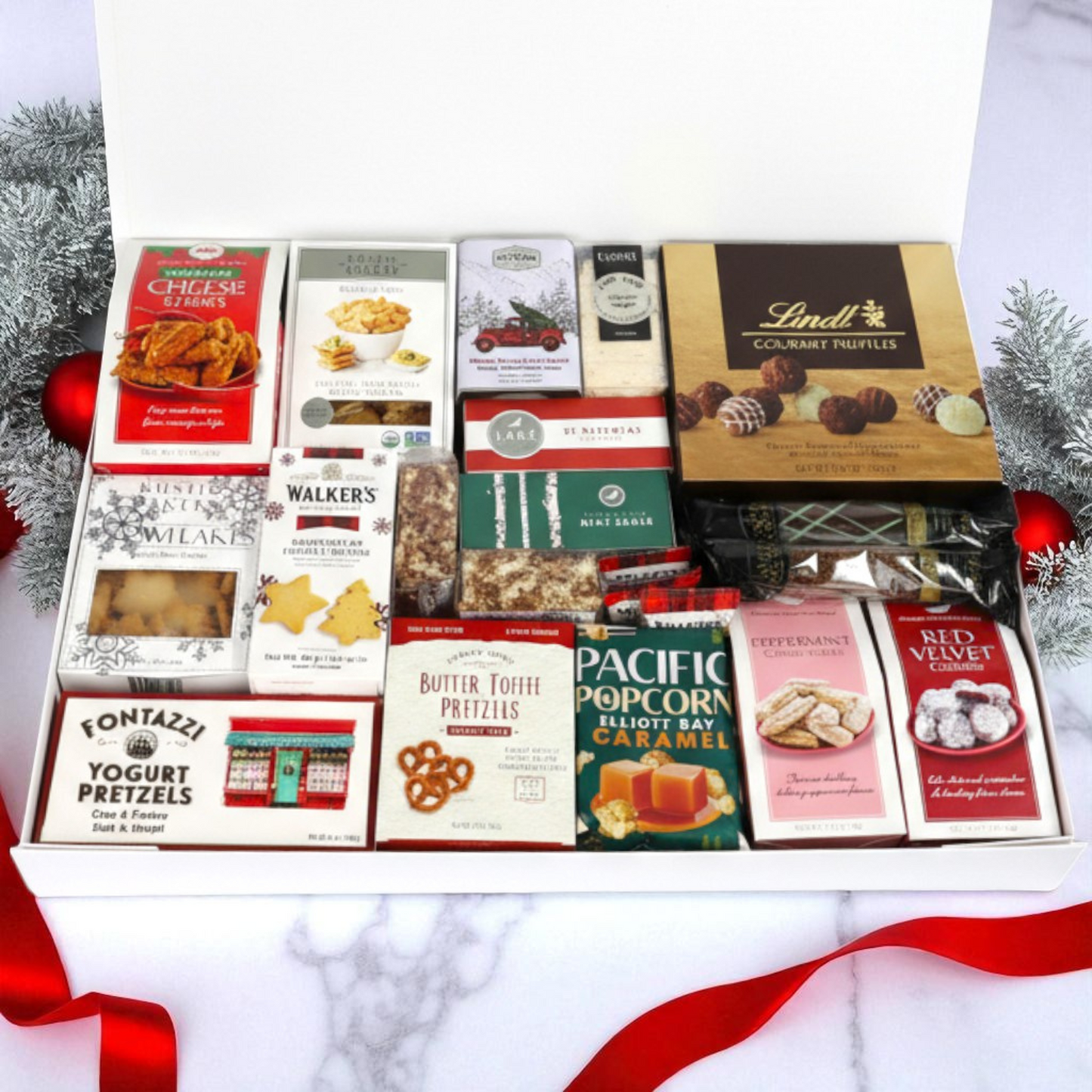 Christmas gourmet gift box with various snacks and treats made in Washington on a white background with red ribbon and Christmas decorations.