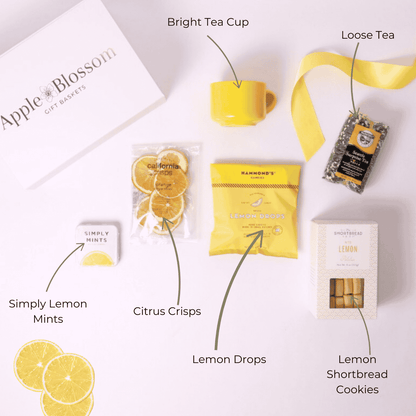 Flat lay image displaying all items in the A Drop of Joy lemon-themed gift box, including lemon shortbread cookies, a ceramic yellow teacup, citrus crisps, Seattle Surprise loose tea, lemon drops, and Simply Lemon mints—perfect for a self-care gift box or tea lover gift set.