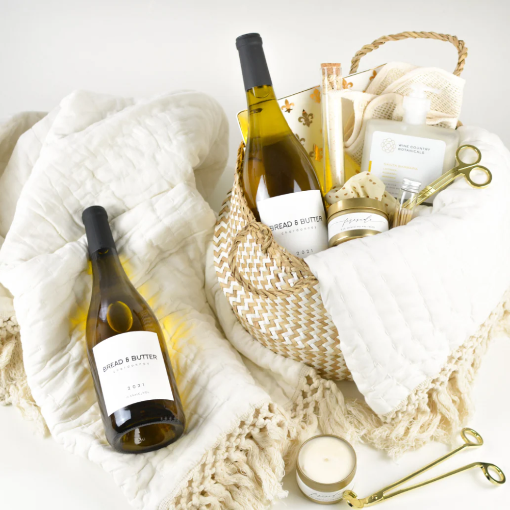 Executive wine and relaxation gift basket with chardonnay, plush throw blanket, soy candle, bath salts, and self care accessories arranged in a woven basket