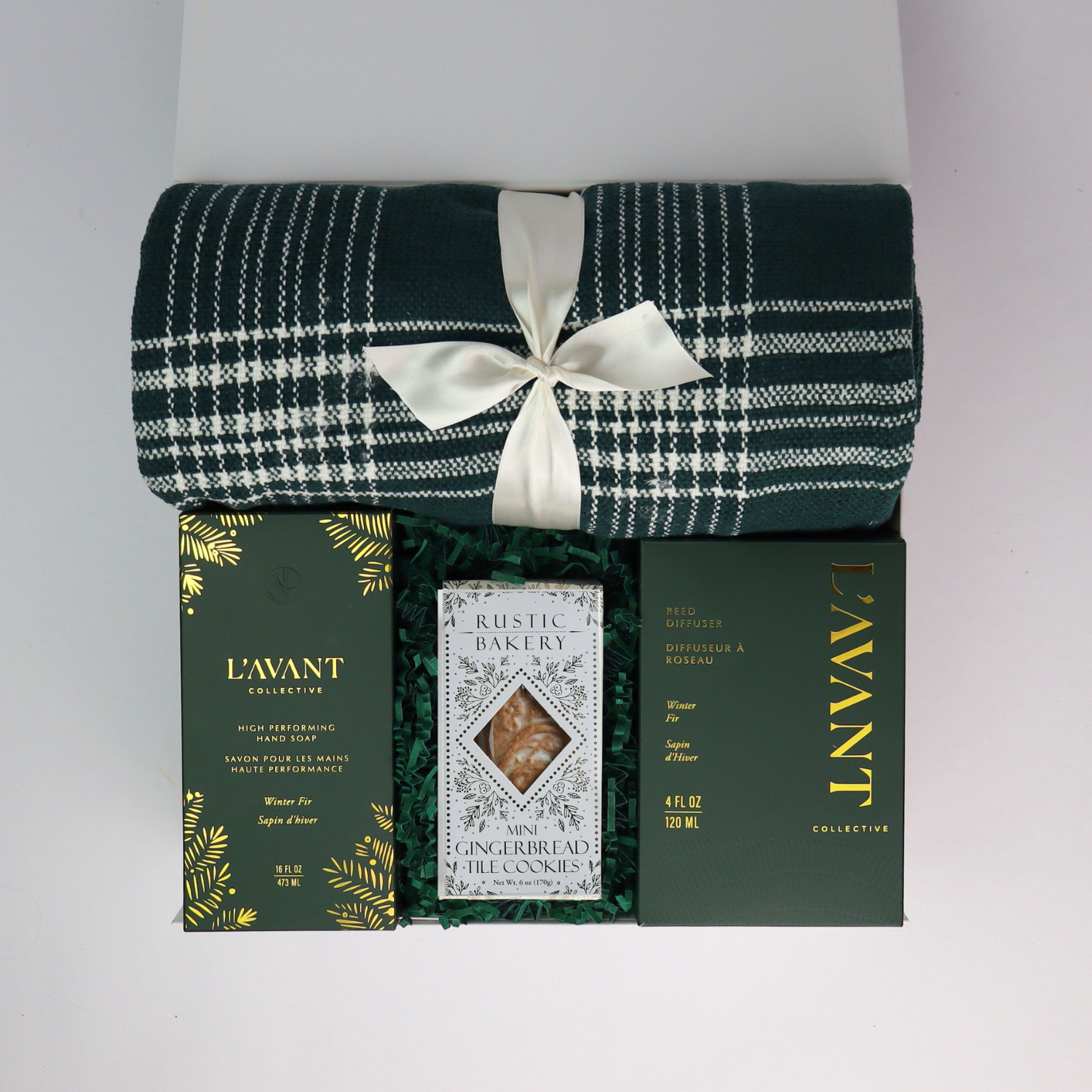 Flat lay of Home for the Holidays gift box with green plaid throw, gold ornaments, and ribbon — made in Washington corporate gift basket.