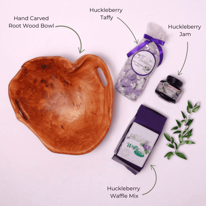 Flat Lay of Huckleberry Gift Basket Contents – A top-down view showcasing wild huckleberry jam, saltwater taffy, waffle mix, and a unique hand-carved wooden bowl, a perfect gourmet food gift.