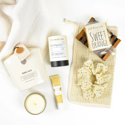Collection of bath and body products including a candle, soap, and scrubber on a white background.