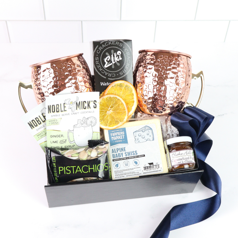 Gift basket with copper mugs, snacks, and moscow mule mix on a white background