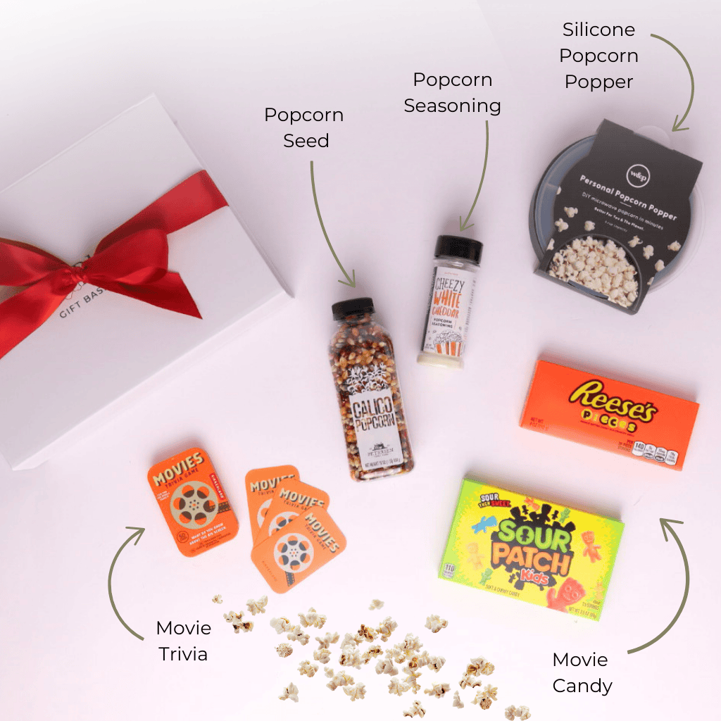 Flat lay of movie night gift basket contents including silicone popcorn popper, candy, popcorn seed and seasoning, and trivia game – cozy gift set for movie lovers.
