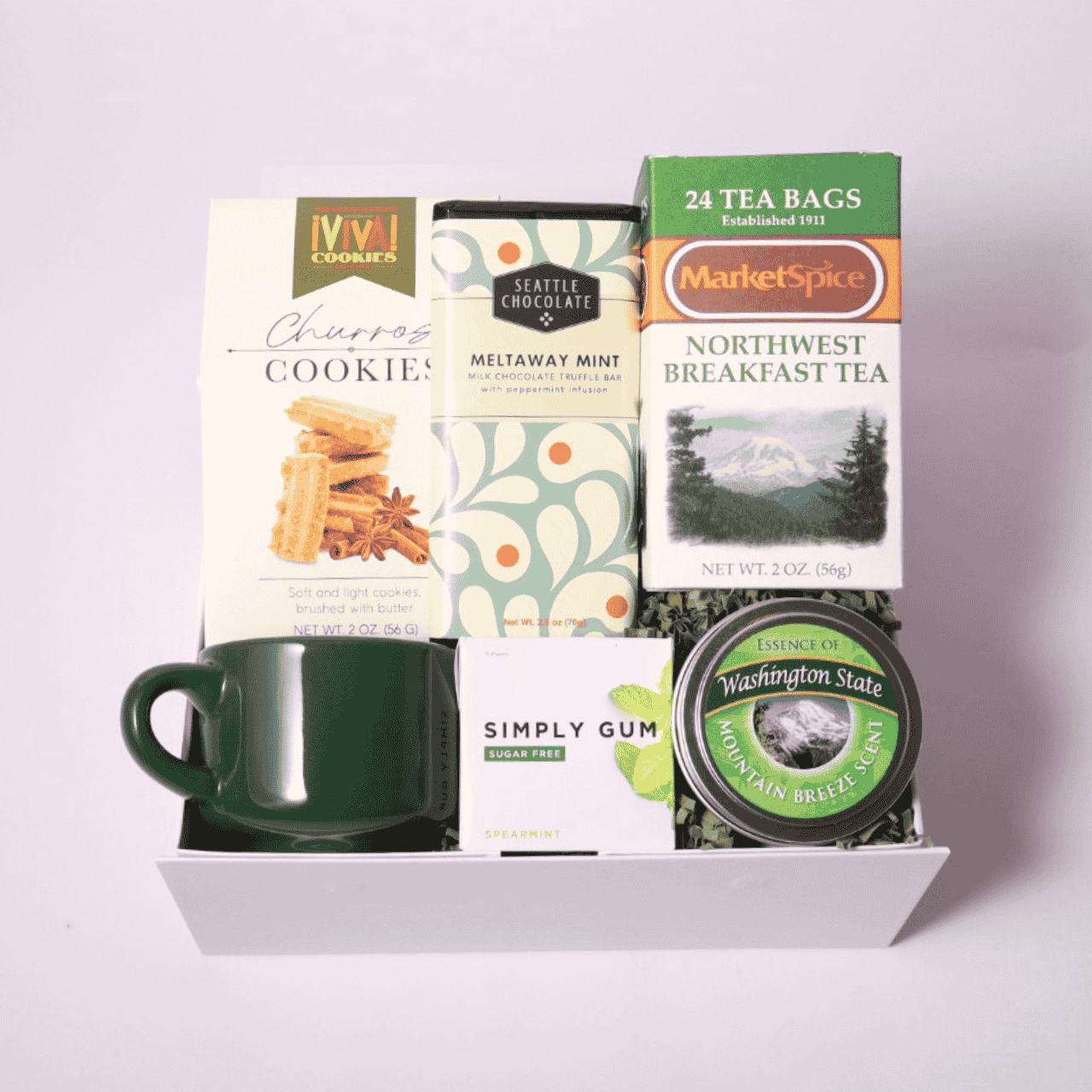 Northwest-themed gift box with a green teacup, MarketSpice tea, soy candle, Seattle Chocolate mint bar, churro cookies, and mints. Ideal for cozying up or gifting a taste of the Pacific Northwest.
