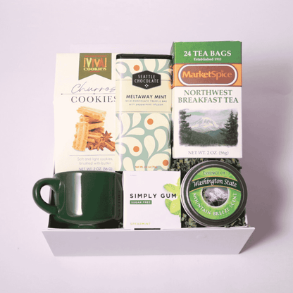 Northwest-themed gift box with a green teacup, MarketSpice tea, soy candle, Seattle Chocolate mint bar, churro cookies, and mints. Ideal for cozying up or gifting a taste of the Pacific Northwest.