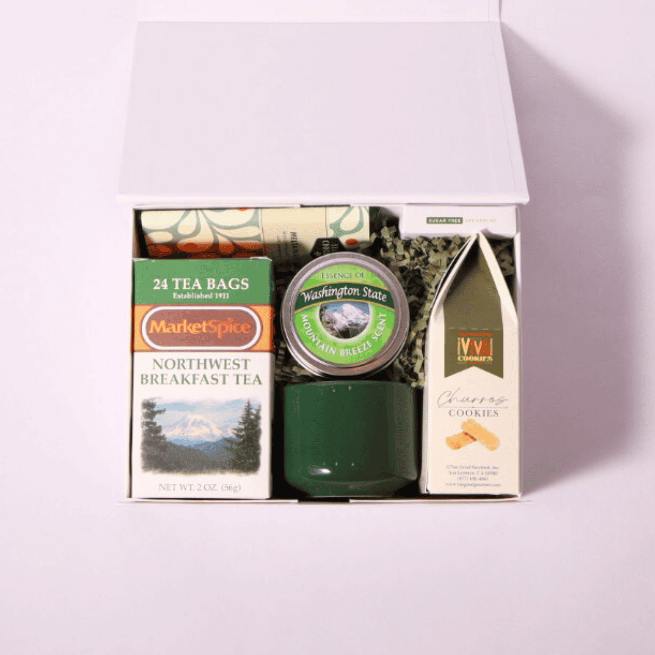 Thoughtful tea-themed gift box with Pacific Northwest-inspired treats and keepsakes: MarketSpice tea, Seattle Chocolate mint bar, soy candle, churro cookies, and green teacup. Great for gifting relaxation.