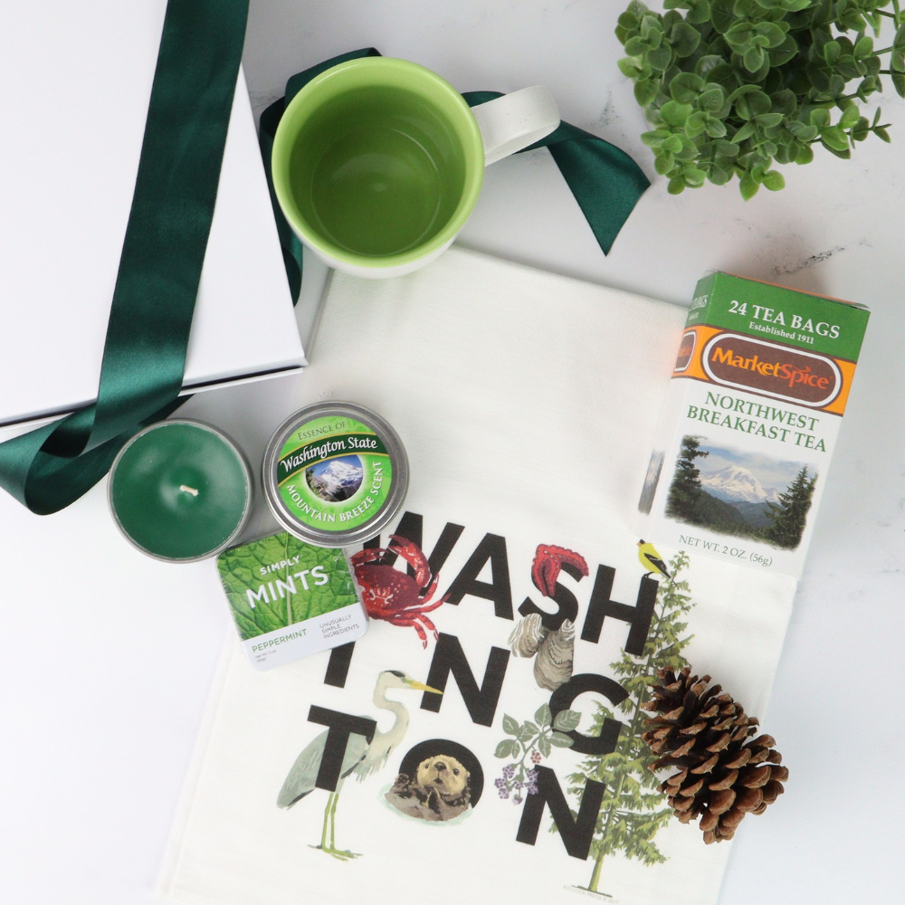 Gift box featuring locally crafted Pacific Northwest treats, including MarketSpice tea, Seattle Chocolate mint bar, soy candle, churro cookies, and a ceramic teacup. Perfect for tea lovers and relaxing break times.