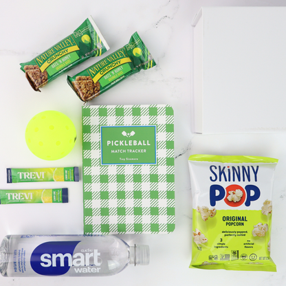 pickelball gift set with a Collection of snacks and a pickleball match tracker on a white surface