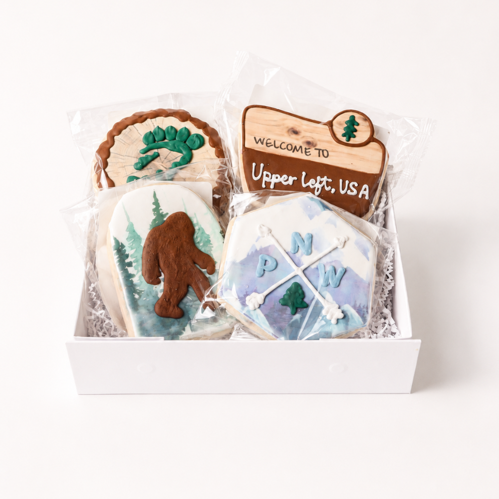Pacific Northwest Cookie Gift Box with four hand-decorated cookies featuring Bigfoot, mountains, evergreen trees, and Upper Left USA design
