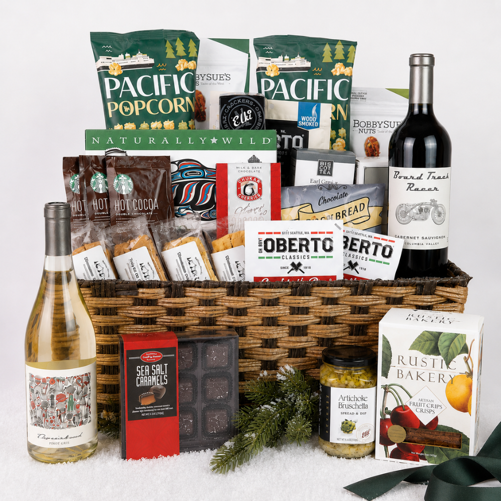A large gourmet gift basket filled with assorted packaged snacks, crackers, chocolates, coffee, a bottle of red wine, and a bottle of white wine, arranged on a white background with decorative greenery and ribbon.