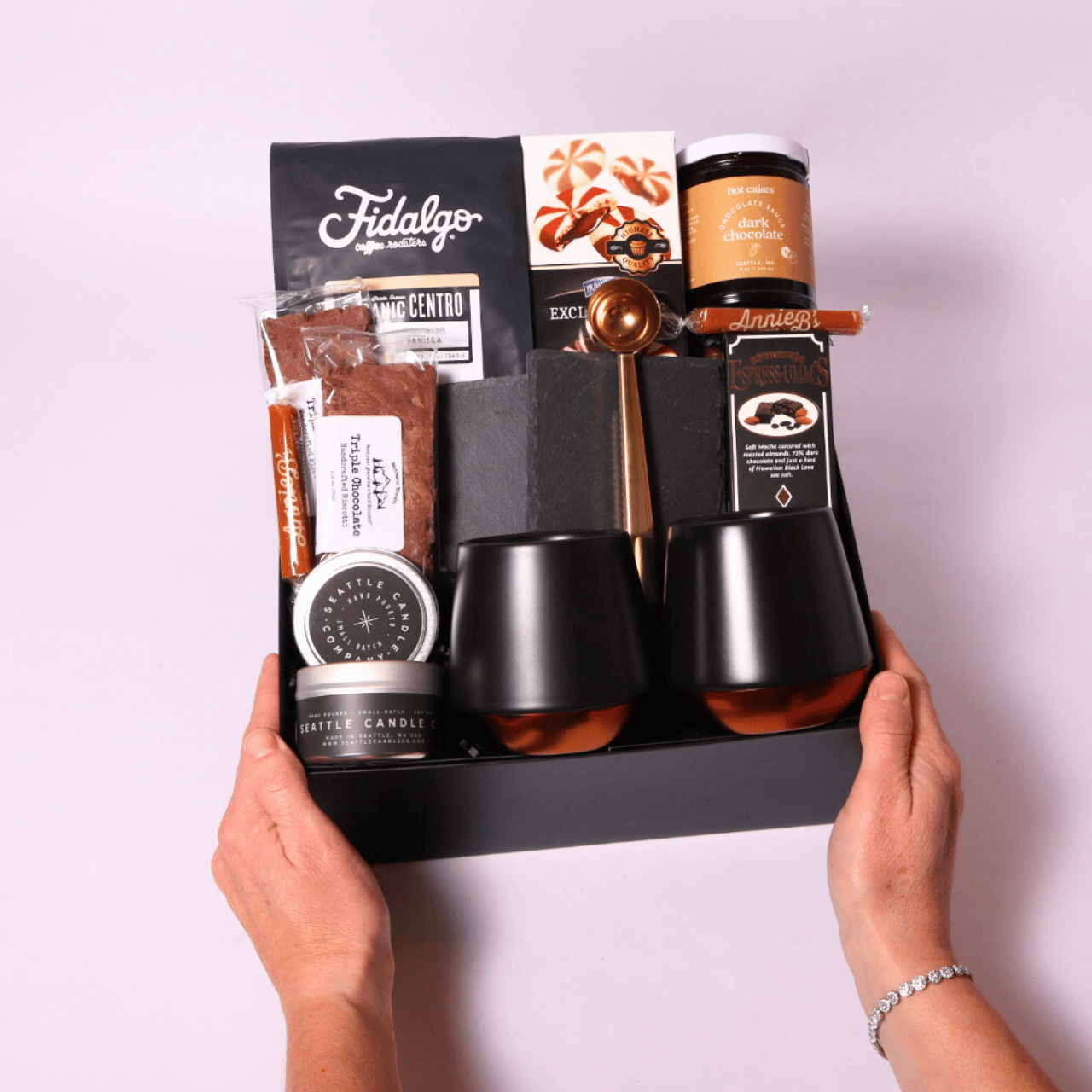 Luxury coffee gift box featuring Fidalgo organic whole bean coffee, Hot Cakes dark chocolate sauce, double-walled Fellow mugs, biscotti, caramels, and more in a sleek black box.