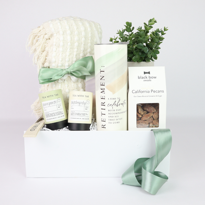 Retirement gift basket for her with cozy blanket, retirement tumbler, gourmet tea, candied nuts, faux plant, and white keepsake box.