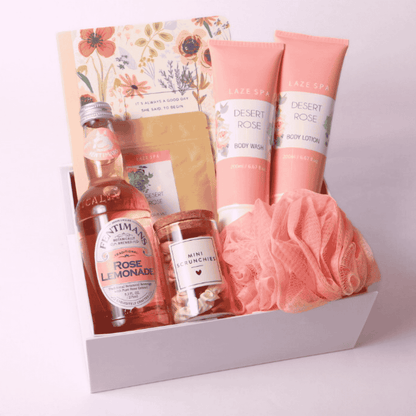 Rose Garden Gift Box with spa and self-care essentials – Includes Fentimans Rose Lemonade, Laze Spa Desert Rose Body Wash and Lotion, a soft pink bath pouf, rose-infused loose tea, a floral notebook, and mini scrunchies in a white gift box. Perfect for relaxation, sympathy, or self-care gifts.