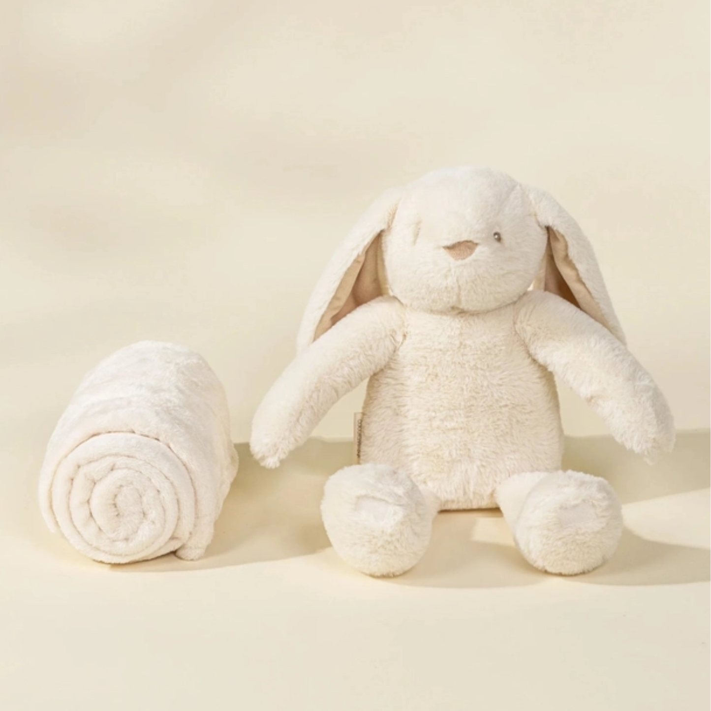 White plush bunny toy next to a rolled-up towel on a beige background