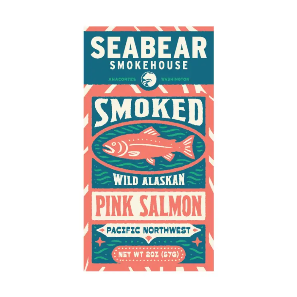 A rectangular package label or box front for Seabear Smokehouse smoked wild alaskan pink salmon, shown on a plain white background. The design uses teal, coral pink, cream, and dark blue with a fish illustration and the text 'Seabear Smokehouse,' 'Smoked,' 'Wild Alaskan,' and 'Pink Salmon.