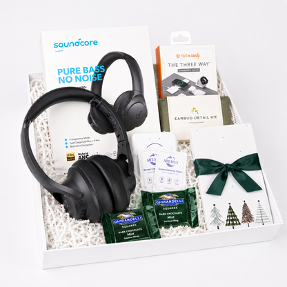 A curated gift box set containing a pair of black Soundcare over-ear headphones, a Soundcore Pure Bass No Noise card, a Nintendo earbud detail kit box, a packet of Ghirardelli chocolate, and a white card tied with a dark green ribbon.