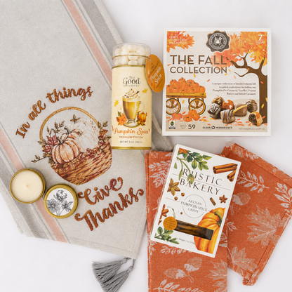 A styled fall-themed gift set on a white background, including a beige embroidered throw blanket with autumn motifs, an orange patterned cloth, a jar of pumpkin spice marshmallows, a box of 'The Fall Collection' marshmallows, and a card for 'Rustic Baker' pumpkin spice latte coffee.
