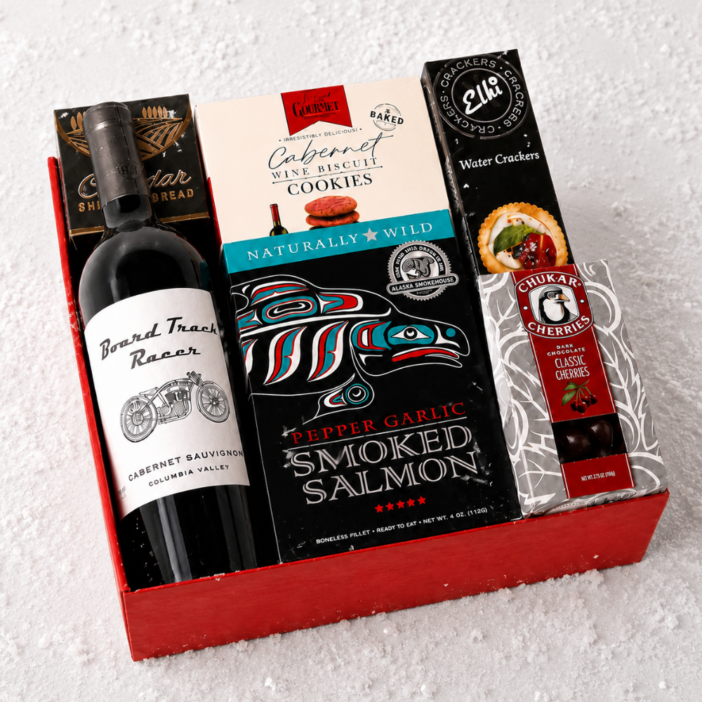 A curated gift box set containing a bottle of Barrel Traces Racer Cabernet Sauvignon, a pack of Pepper Garlic Smoked Salmon, a box of Chukar Gourmet Water Crackers, and a bag of Chukar Gourmet Pepper Jack Bread, all arranged in a red gift box on a white textured background.