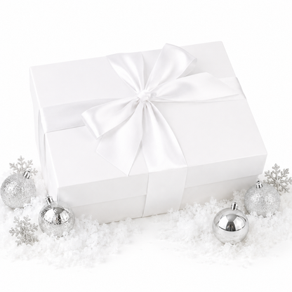 A white gift box wrapped with a large white satin ribbon and bow, styled on a white surface with scattered faux snow and silver holiday ornaments.
