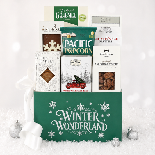 A holiday gift basket filled with assorted packaged snacks and treats, set in a snowy studio scene. The green basket lid reads “Winter Wonderland,” and visible packages include Pacific Popcorn, Sugar & Spice Pretzels, Rustic Bakery cookies, and others.